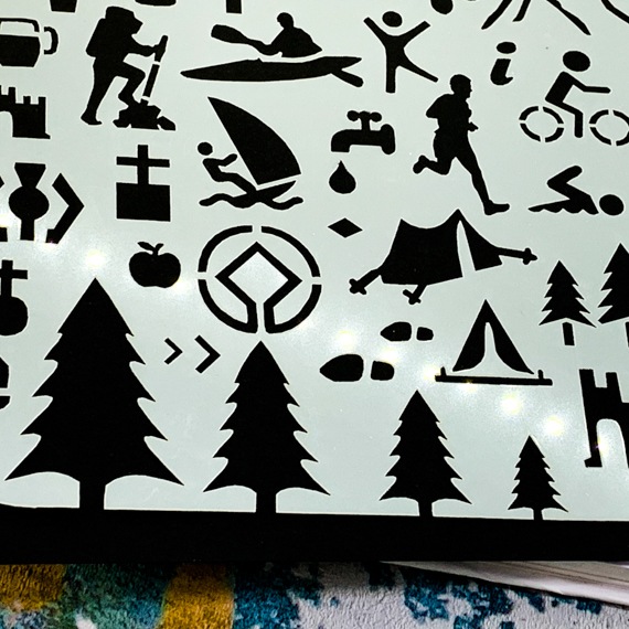 Adventures Journal Stencil, Travel A5 Journal Sized Stencil with adventure activity shapes & OS Symbols, craft mylar stencil - Close up of bottom left, showing pine trees, OS Map Symbols, camping tent, wind surfing, church, canoe, hiker, runner, tap, beer, castle, footsteps, apple, tent