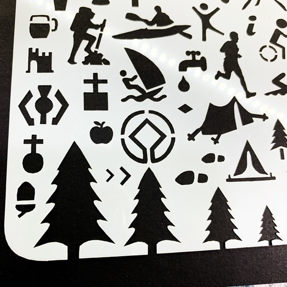 Adventures Journal Stencil, Travel A5 Journal Sized Stencil with adventure activity shapes & OS Symbols, craft mylar stencil - Close up of bottom left, showing pine trees, OS Map Symbols, camping tent, wind surfing, church, canoe, hiker, runner, tap, beer, castle, footsteps, apple, tent