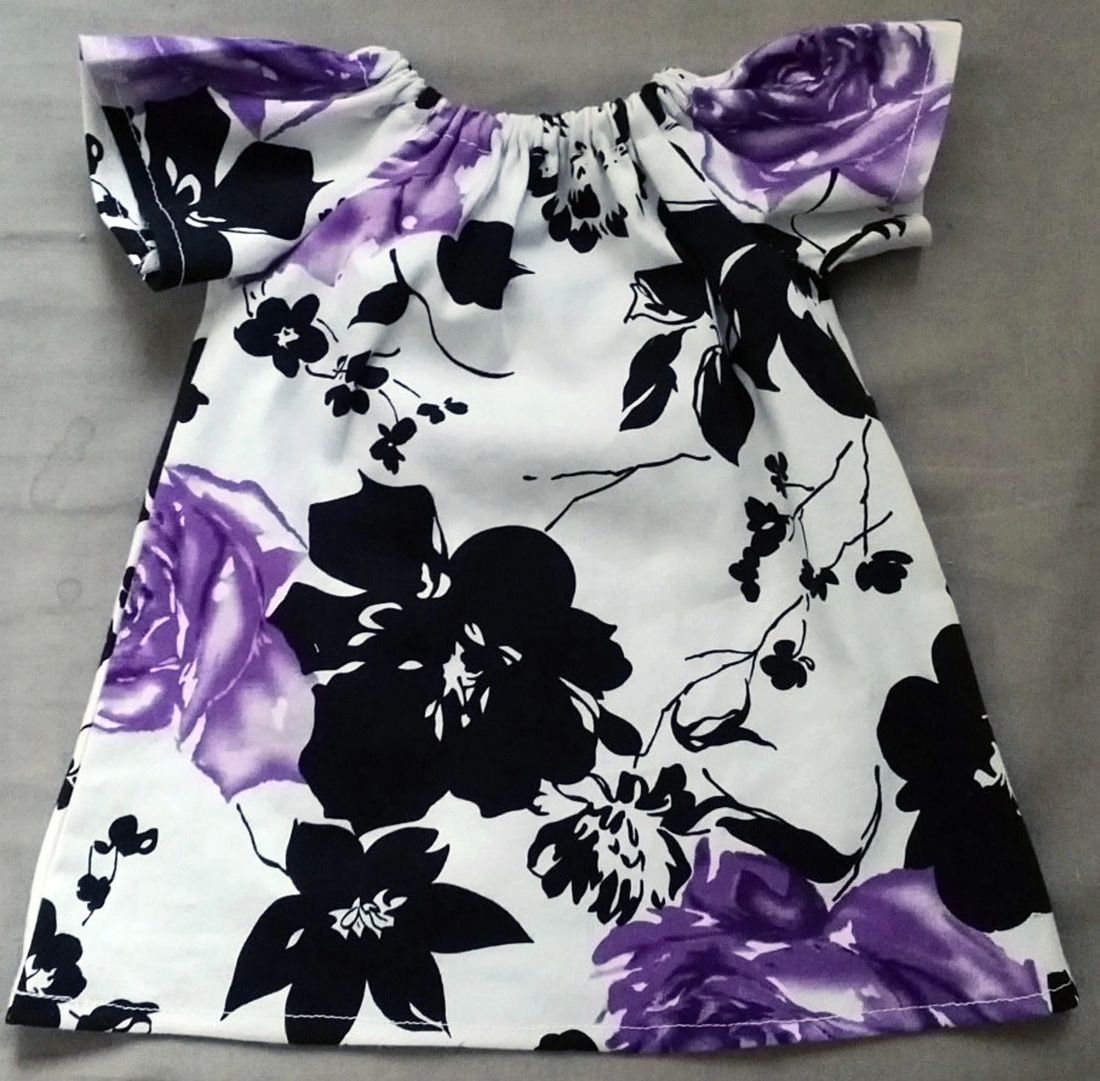 An upcycled newborn dress with purple and black floral pattern