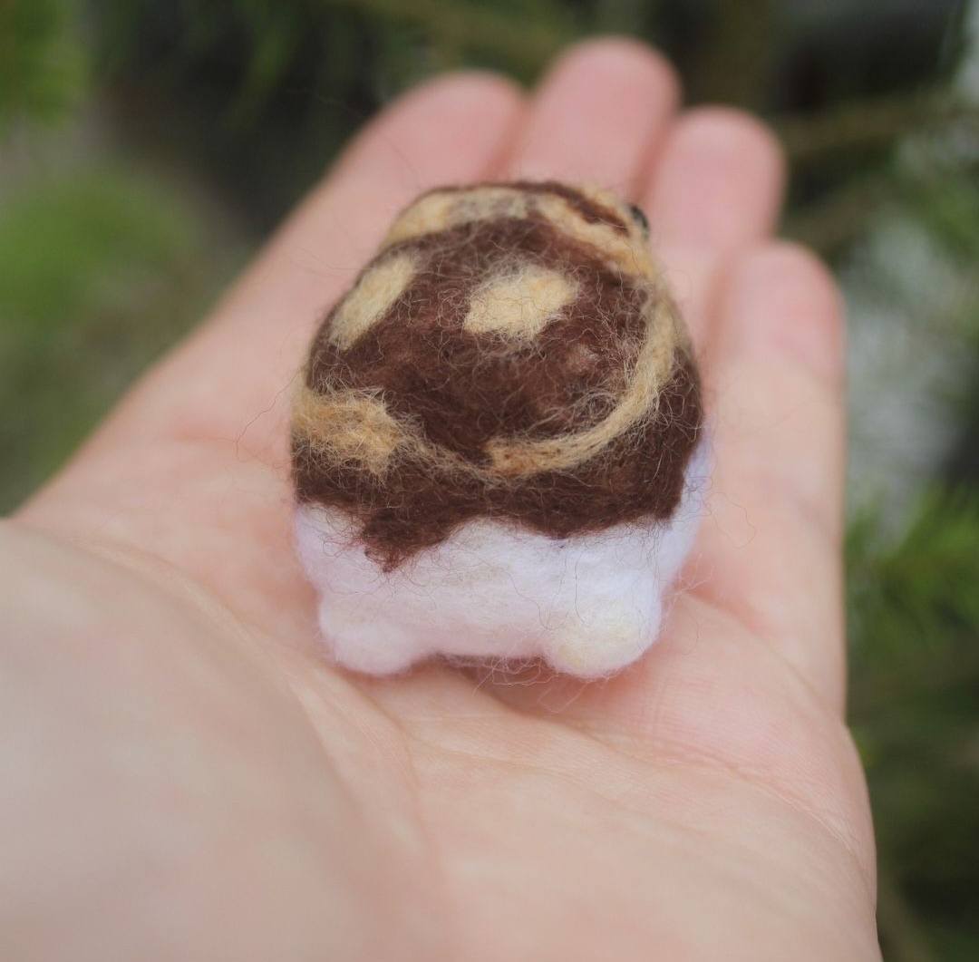 A small rain frog sits upon a hand, it is dark brown with light brown accents. It has a white bottom half and can be seen here from the back