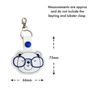 Bear Face with Glasses Keyring featuring an embroidered bear face with blue glasses on white faux leather, shown with approximate measurements of 75mm height and 66mm width, excluding the keyring and lobster clasp.