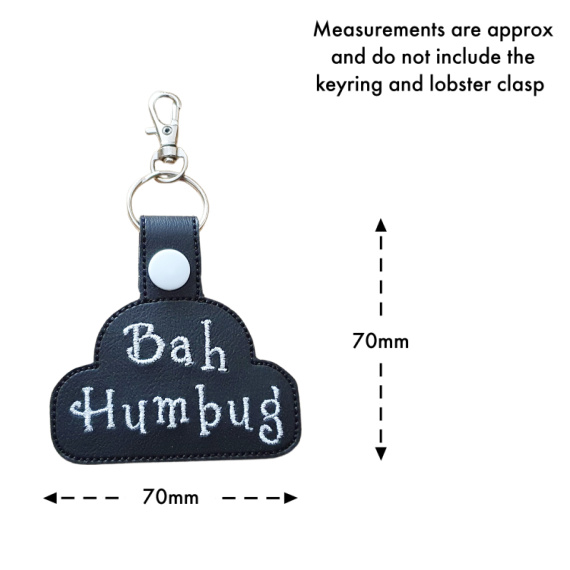 black faux leather keyring embroidered with the words ‘Bah Humbug’ in white thread, shown with a white snap fastener and metal clasp. Measurement markers indicate approximately 70mm by 70mm, not including the keyring and clasp.