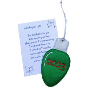 Green felt Christmas light bulb ornament with silver top, embroidered with ‘2023,’ displayed alongside a blue poem card titled ‘A Colleague’s Light.’