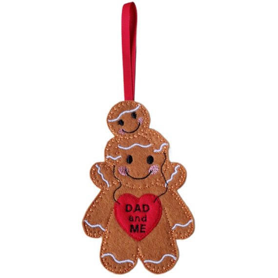 Handmade felt Dad and Me Gingerbread Character showing a large gingerbread dad with a smaller girl gingerbread on his shoulders, both smiling with pink cheeks, holding a red heart reading “Dad and Me,” finished with a red ribbon for hanging.