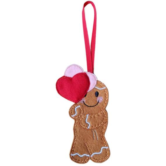 Handmade felt gingerbread character with stitched details and smiling face, holding two heart balloons—front balloon red, back balloon pink. Finished with a red ribbon loop for hanging.