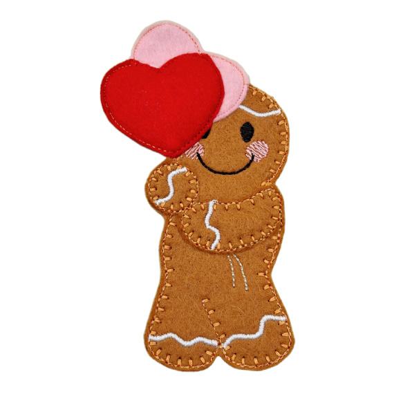 Handmade felt gingerbread character holding two heart balloons, back balloon is pink and front balloon is red.