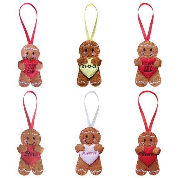 Six handmade felt gingerbread hanging decorations, each holding a heart with different embroidered text. Messages include 'I LOVE YOU DAD,' a date '09-12-21,' 'I LOVE YOU MUM,' and personalised names such as 'Ellen,' 'Kerrie,' and 'Becci.' Each gingerbread has stitched icing details, a smiling face, and a ribbon loop in various colours for hanging.