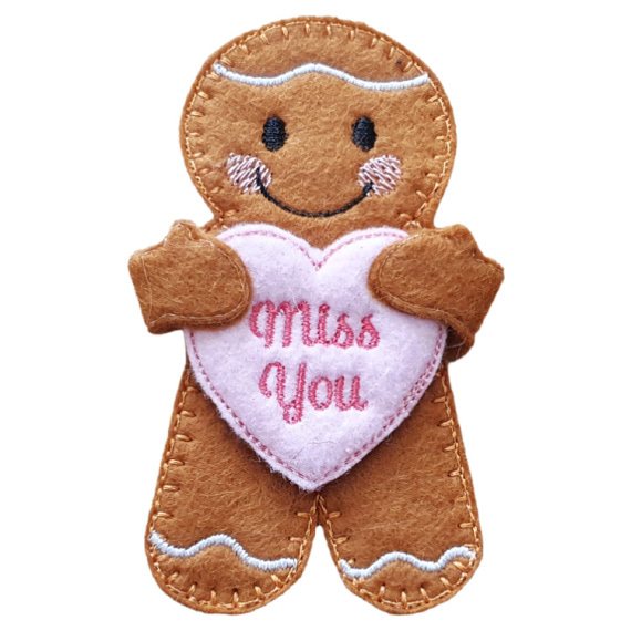Handmade felt gingerbread character with stitched icing details, rosy cheeks, and a smiling face. The gingerbread is holding a pale pink heart embroidered with the words 'Miss You' in red thread.