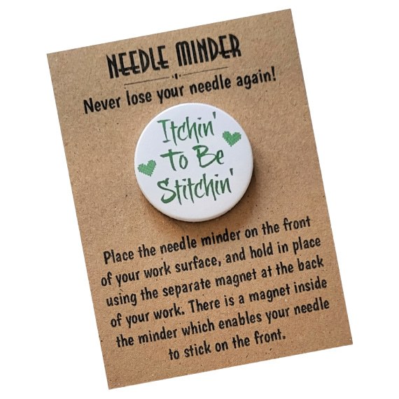 Round magnetic needle minder with bright green text that reads ‘Itchin’ To Be Stitchin’’ and two small green stitched-style hearts, on a white background. Displayed on kraft card packaging with instructions.