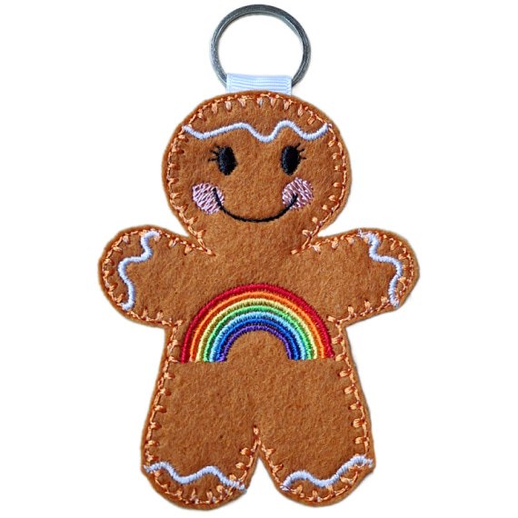 Rainbow Smiles Gingerbread Character – female version. A cheerful felt gingerbread keyring with delicate embroidered eyelashes, a vibrant rainbow across its front, smiling face, and white icing details, finished with a silver keyring loop to carry with pride.