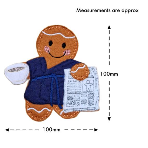 Rise and Shine Gingerbread Character — a handmade felt gingerbread figure wearing a navy blue dressing gown, smiling while holding a white cup of tea or coffee in one hand and a stitched newspaper in the other. Approximate measurements are shown as 100mm in height and 100mm in width.