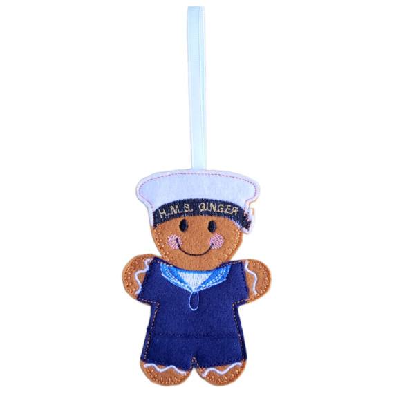 Royal Navy Sailor Gingerbread Character in a dark blue sailor uniform with a light blue collar and a white cap embroidered with ‘HMS GINGER.’ The decoration is finished with a white ribbon loop for hanging.