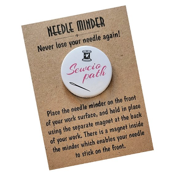 Round 38mm needle minder with the word “Sewciopath” in pink script, decorated with a spool of thread and needle graphic, shown on kraft backing card.