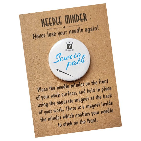 Round 38mm needle minder with the word “Sewciopath” in turquoise script, featuring spool of thread and needle illustration, packaged on kraft backing card.