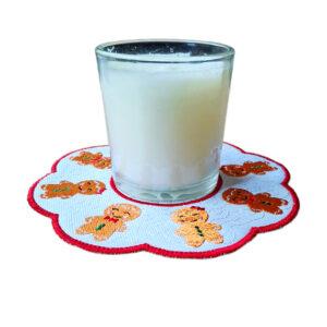 Glass candle holder placed on Smiling Gingerbread Friends Decorative Table Mat, embroidered Christmas table mat with gingerbread design