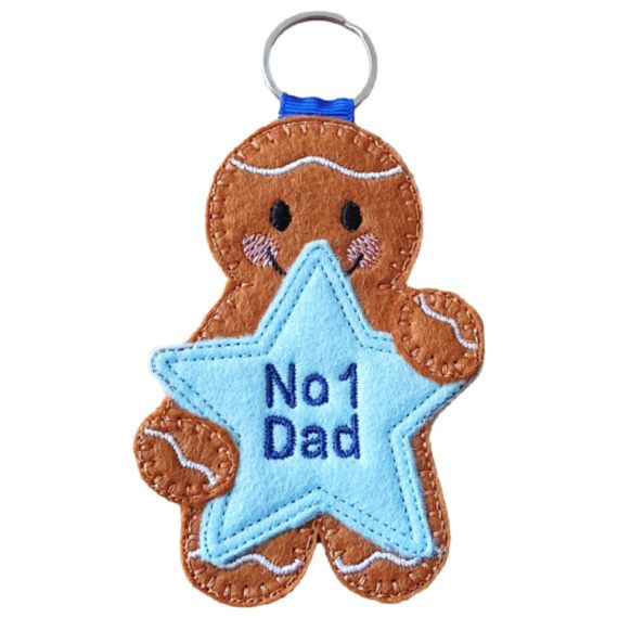 Handmade felt gingerbread character holding a blue star with embroidered text ‘No1 Dad.’ Finished as a keyring with silver metal ring and blue ribbon loop.