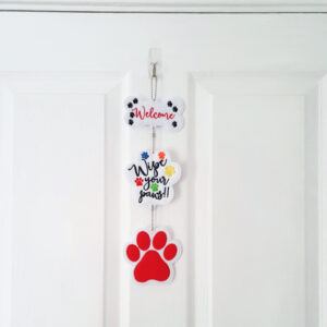 Full view of the Welcome ‘Wipe Your Paws’ Decoration hanging from a hook on a white door, showing three felt panels joined by a chain: a bone with “Welcome,” a paw with “Wipe your paws!!” and a red pawprint at the bottom.