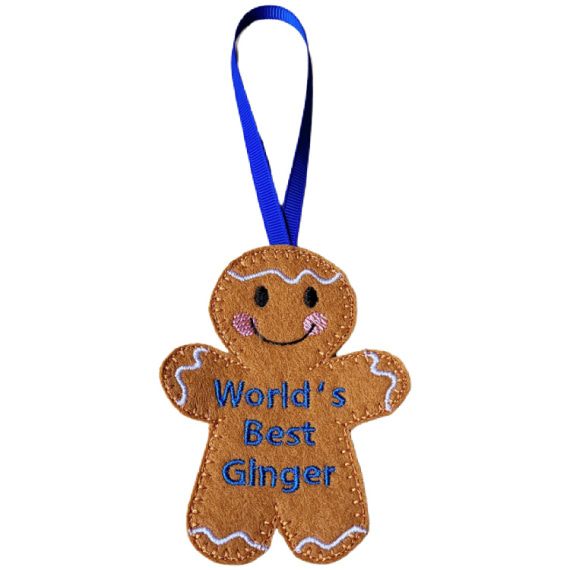 World’s Best Ginger Gingerbread Character — a handmade felt gingerbread figure with a smiling face, rosy cheeks, and blue embroidered text reading “World’s Best Ginger.” A blue ribbon loop is attached for hanging.