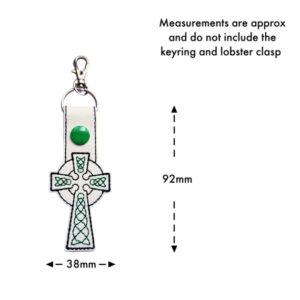 White faux leather Celtic Cross keyring with green embroidery, green snap button, and metal clasp. The image includes measurements showing 92mm in height and 38mm in width, with a note stating measurements do not include the keyring or lobster clasp.