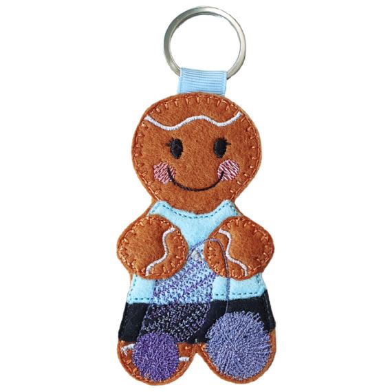 A felt crochet gingerbread character keyring with a metal ring, featuring a smiling face, cosy stitched details, a pale blue top, black skirt, and balls of yarn.