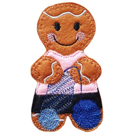 A smiling felt crochet gingerbread character with cosy stitched details, a pink top, black skirt, and balls of yarn, shown without hanging loop or attachments.