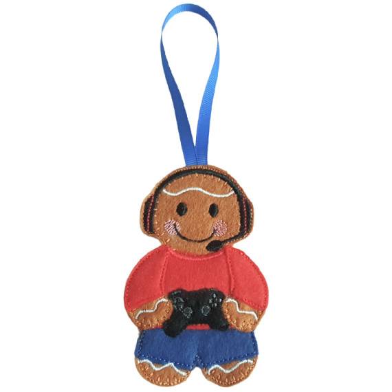 A felt gamer gingerbread decoration with a blue hanging ribbon, wearing a red top and blue trousers, smiling while holding a small black game controller.