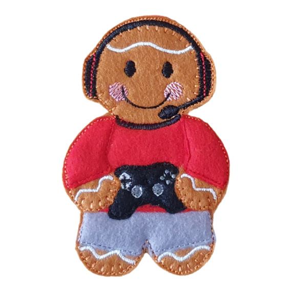 A felt gamer gingerbread character wearing a red top, grey trousers, and a black gaming headset, smiling while holding a small black game controller.
