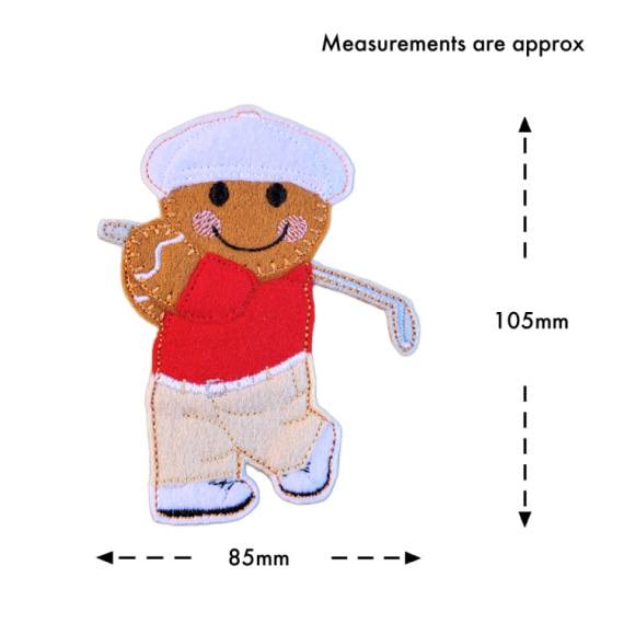 A felt golfer gingerbread character wearing a red shirt, beige trousers, white shoes, and a white cap, smiling and holding a small golf club in a swinging pose. The character measures approximately 105 mm tall and 85 mm wide.