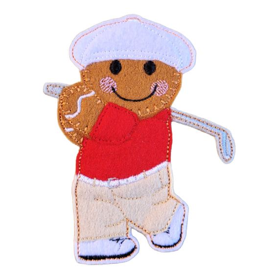 A felt golfer gingerbread character wearing a red shirt, beige trousers, white shoes, and a white cap, smiling while holding a small golf club in a swinging pose.
