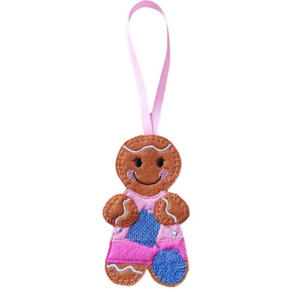 A felt knitting gingerbread character hanging decoration with a pink ribbon loop, featuring a smiling face, cosy stitched details, a pink top, patterned skirt, and a ball of yarn.
