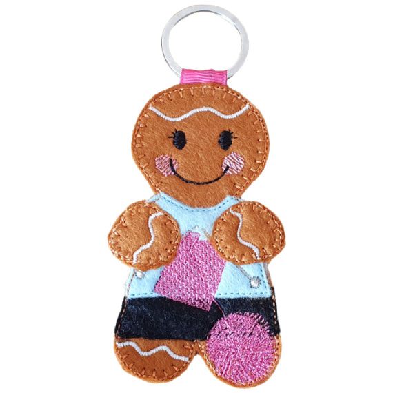 A felt knitting gingerbread character keyring with a metal ring, featuring a smiling face, cosy stitched details, a pale blue top, patterned skirt, and a ball of yarn.