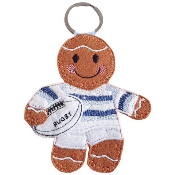 Felt gingerbread rugby player character wearing a white kit with blue hoops, holding a white rugby ball stitched with the word “Rugby,” shown with a metal keyring loop attached at the top.