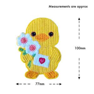 Smiling felt chick holding flowers and a small envelope with a heart, machine embroidered with a knit stitch pattern, shown on a white background with approximate measurements of 77mm wide and 100mm tall.