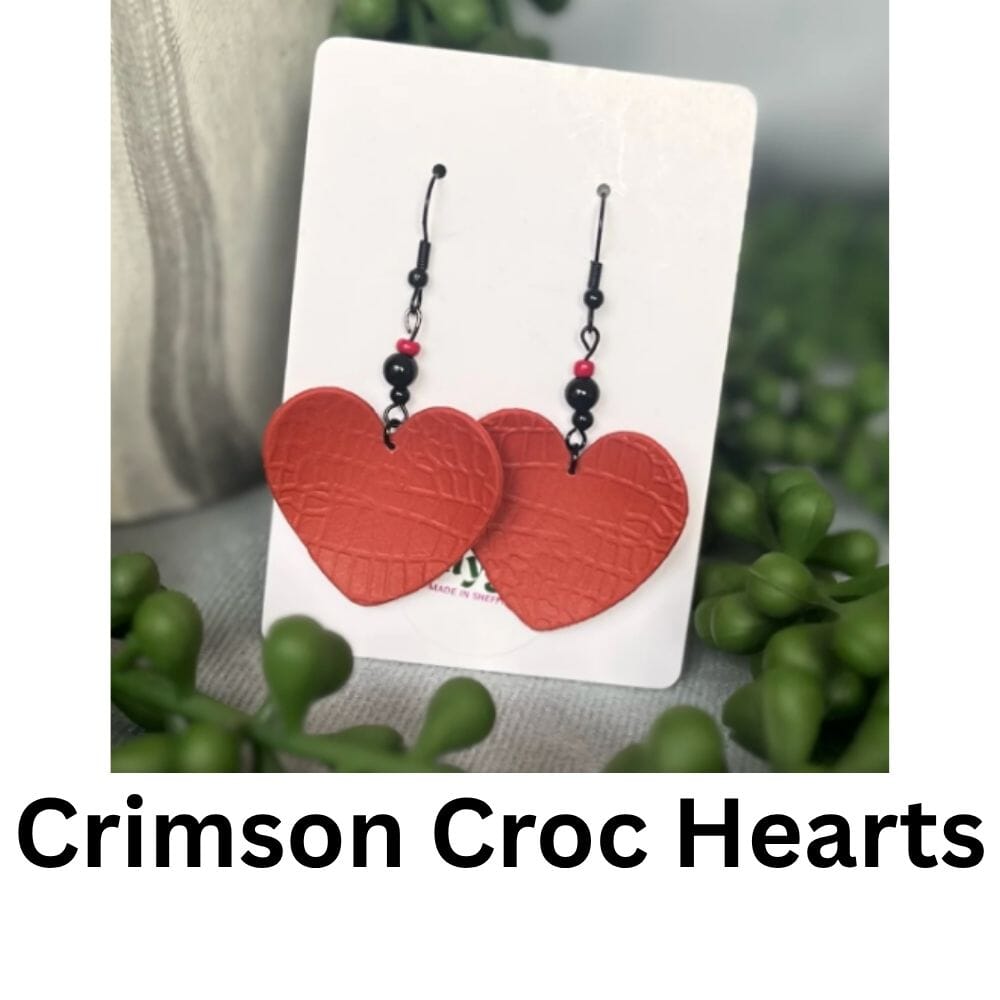 Heart-shaped red crocodile-textured polymer clay earrings with black bead accents, handmade in Sheffield and displayed on a Lollygag card.