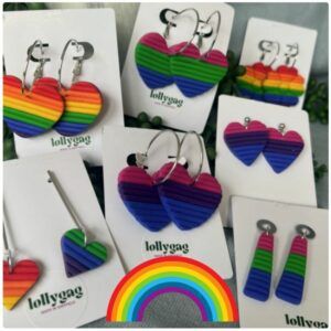 Custom Pride earrings by Lollygag displayed as a group, handmade polymer clay earrings in heart, flower and flag shapes with horizontal LGBTQ+ Pride flag stripes, lightweight stainless steel findings, handmade in Sheffield.