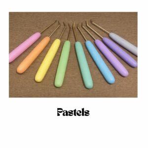 Custom loom hooks with smooth plain colour polymer clay handles in soft pastel shades including pink, peach, yellow, mint, blue and lilac, arranged on a wooden surface.