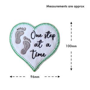 Embroidered felt heart decoration with footprints and the words ‘One Step at a Time’, shown with approximate measurements of 100mm high and 96mm wide.