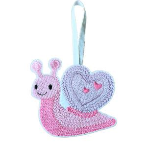 Smiling felt snail with a heart-shaped shell, machine embroidered with a knit stitch pattern and hanging from a ribbon on a white background