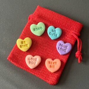 Handmade polymer clay love tokens in pastel colours with embossed sparkly love heart phrases, presented in a small red drawstring pouch, Valentine’s gift and wellbeing fidget tokens by Lollygag