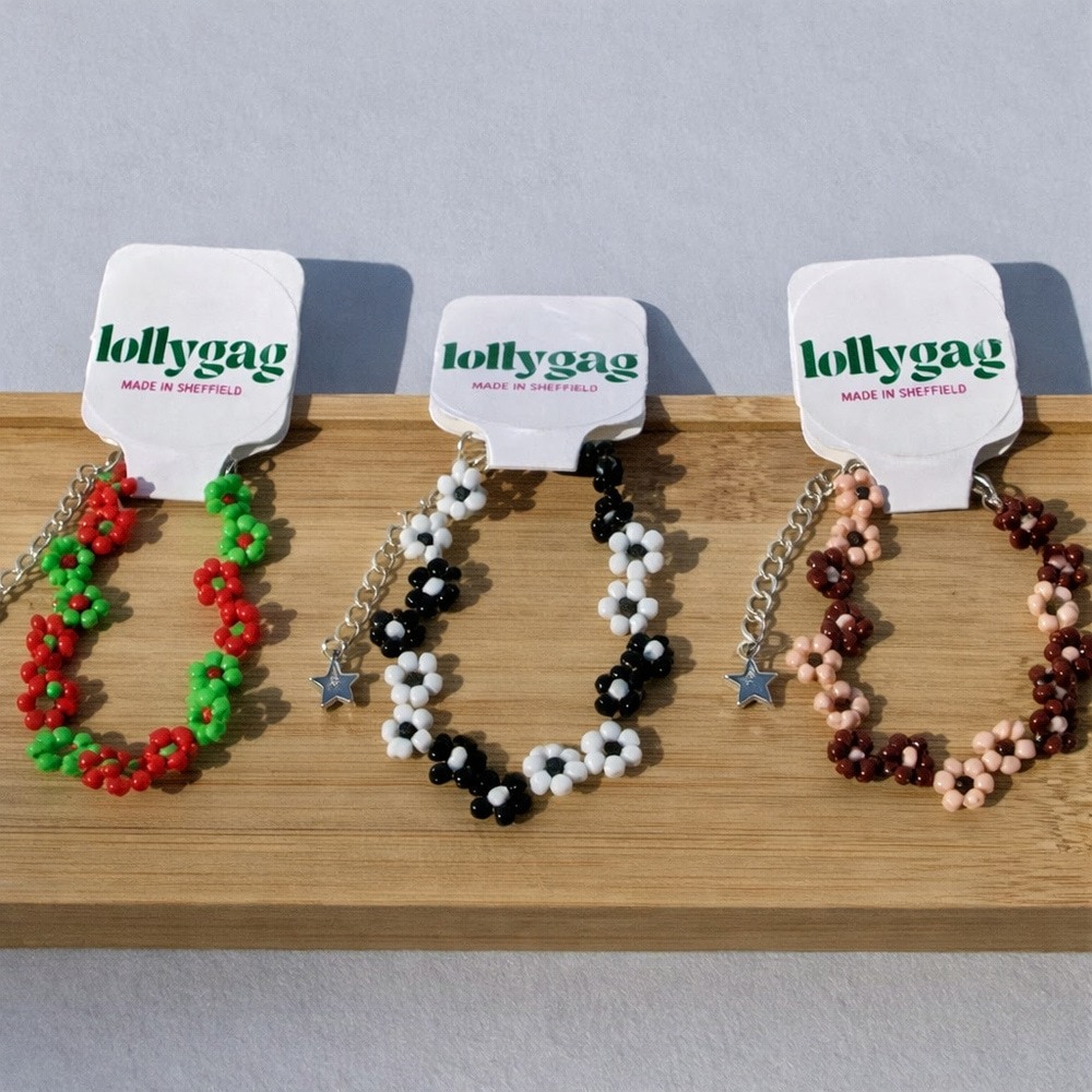 Three handmade beaded flower chain bracelets by Lollygag displayed on a wooden stand, in red and green, black and white, and brown and blush colourways, made in Sheffield.