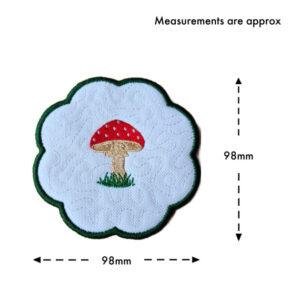Round scalloped toadstool candle coaster with central embroidered mushroom design, shown with measurement guide indicating approximately 98mm width and 98mm height.