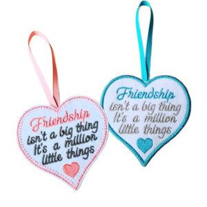 Two heart-shaped felt hanging decorations shown side by side, each with a ribbon loop. Both hearts feature an embroidered friendship message reading, ‘Friendship isn’t a big thing, it’s a million little things’, with a small decorative heart detail.