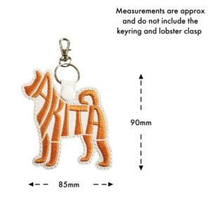 Embroidered Akita word art keyring on white faux leather with orange embroidery, measuring approximately 85mm wide and 90mm high, excluding the keyring and lobster clasp.