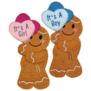 Two felt gingerbread decorations holding heart-shaped balloons. One gingerbread holds pink and dark pink hearts with the words ‘It’s A Girl’, and the other holds blue and light blue hearts with the words ‘It’s A Boy’. Both have stitched icing details, rosy cheeks, and smiling faces.