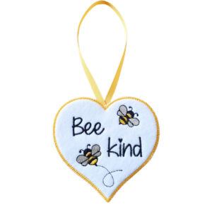 White felt heart-shaped hanging decoration with the words “Bee kind” embroidered in black, featuring two small embroidered bees. The heart has a yellow stitched border and hangs from a matching yellow ribbon loop against a white background.