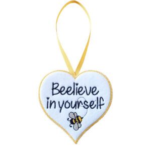White felt heart-shaped hanging decoration with the words “Beelieve in yourself” embroidered in black, featuring a small embroidered bee. The heart has a yellow stitched border and hangs from a matching yellow ribbon loop against a white background.