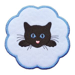 Embroidered candle coaster with a scalloped edge, featuring a black cat face with blue eyes and a pink nose in the centre on a white background with blue edging.