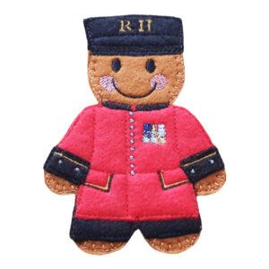 Chelsea Pensioner Gingerbread Character made from felt, wearing a red coat with black trim and embroidered medals, and a matching black hat with gold “R H” lettering.