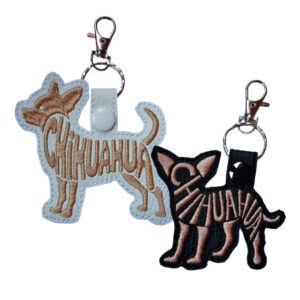 Two faux leather Chihuahua word art keyrings, one in white with tan embroidery and one in black with light stitching, each featuring the word “Chihuahua” forming the dog’s shape and finished with a metal clasp and snap fastening.