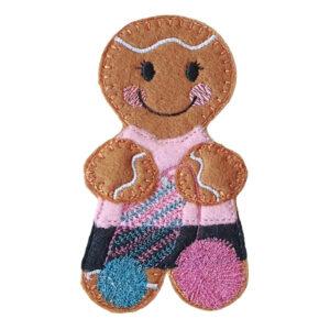 A smiling felt crochet gingerbread character with cosy stitched details, a pink top, patterned skirt, and balls of yarn.